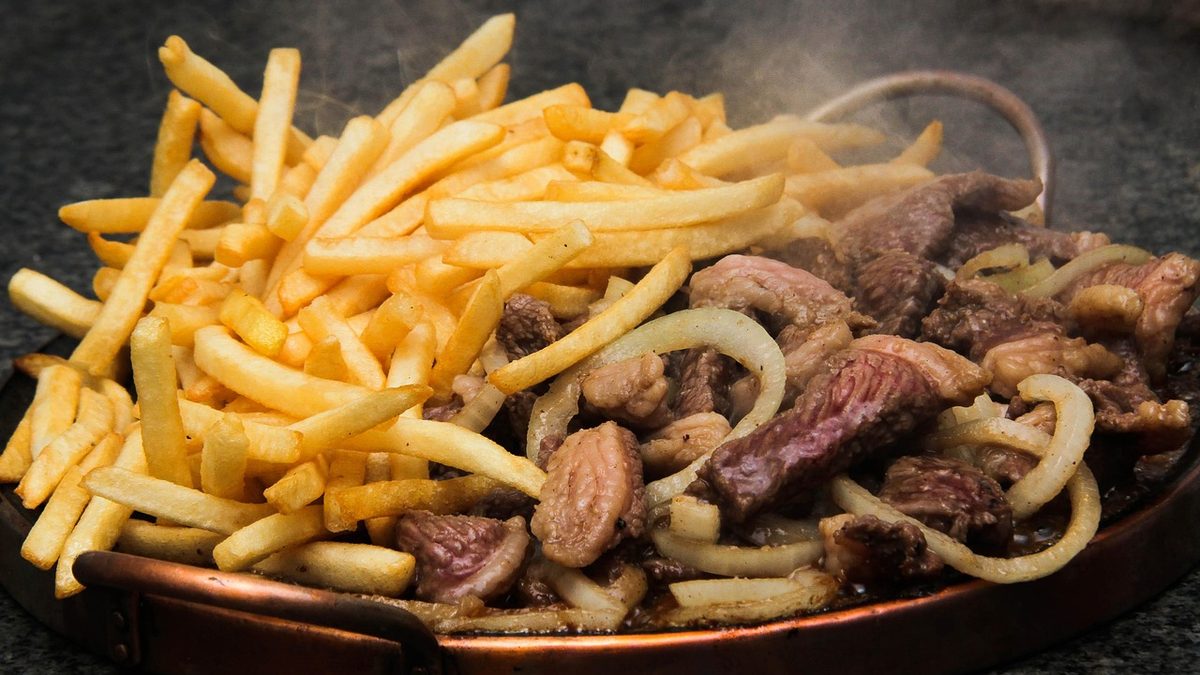 Porção de carne acebolada com batatas fritas em travessa de cobre