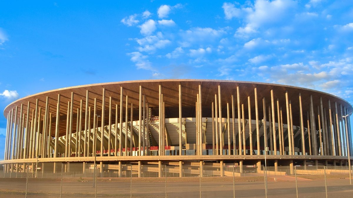 Fachada do Estádio Nacional Mané Garrincha, com pilares brancos, sob céu azul em Brasília