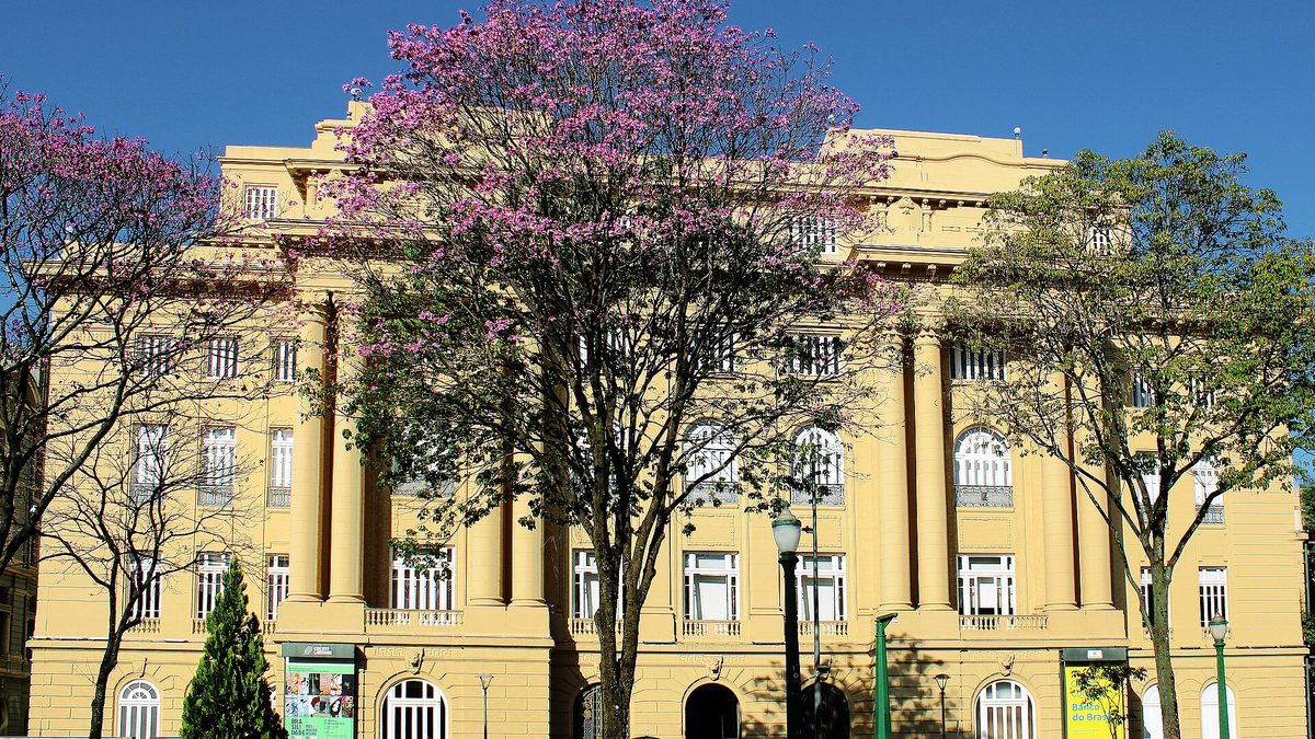 Prédio amarelo do CCBB na Praça da Liberdade, com ipê roxo florido, em Belo Horizonte