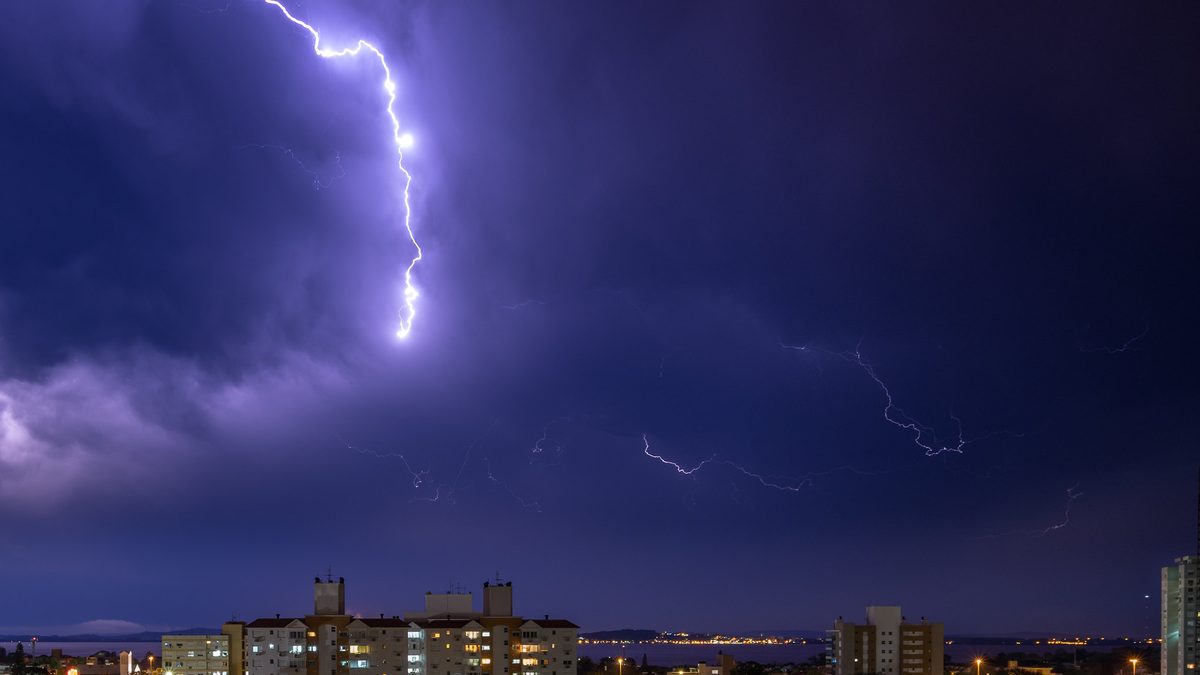 Raio corta o céu noturno sobre prédios de Porto Alegre durante tempestade