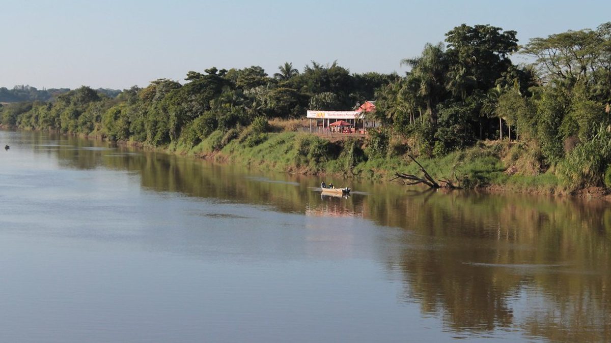 Barco no rio Ribeira de Iguape, com mata e um quiosque na margem, em Registro