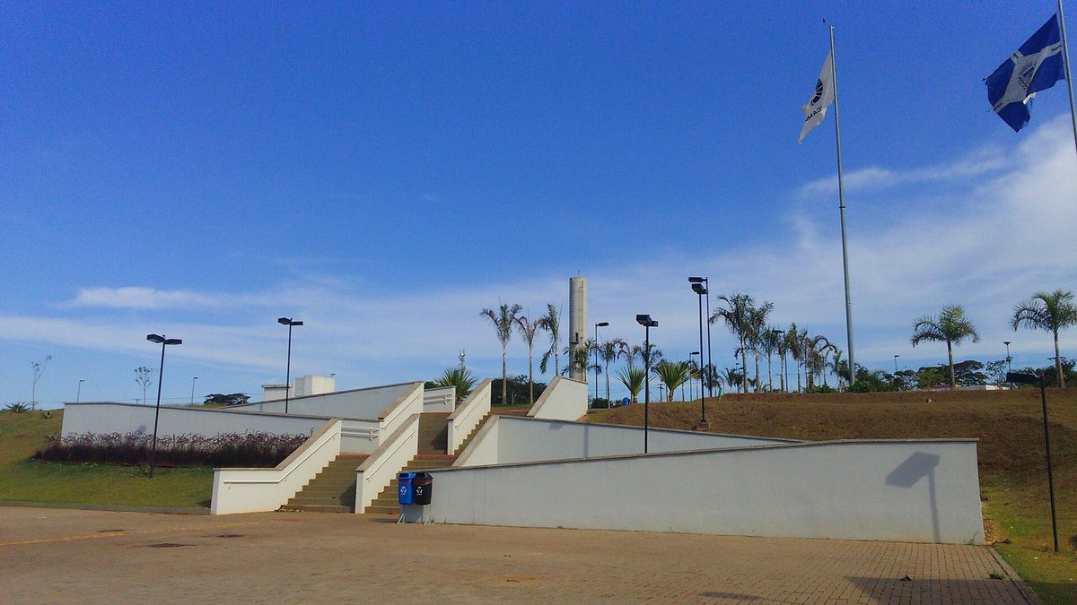 Escadaria, bandeiras e palmeiras no campus da Unicamp em Limeira, sob céu azul