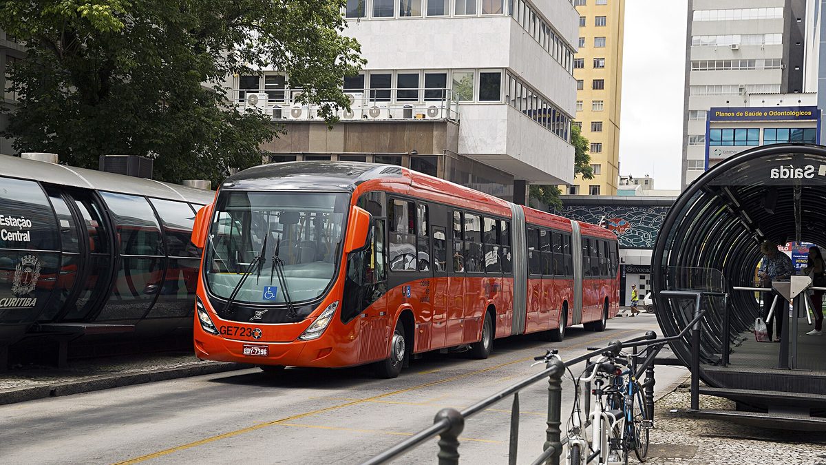 Ônibus biarticulado vermelho para em estação-tubo numa canaleta de Curitiba